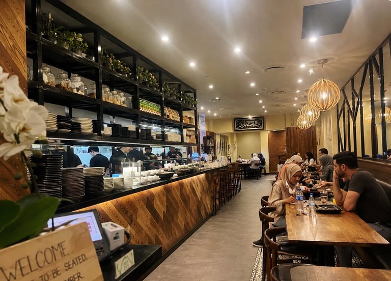 Modern coffee shop interior with counter, shelving, customers seated at table, and pendant lighting
