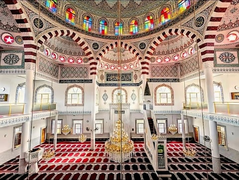 Interior of the Auburn Gallipoli Mosque with ornate Islamic architecture, red and white arched ceilings, colourful stained glass windows and a central chandelier