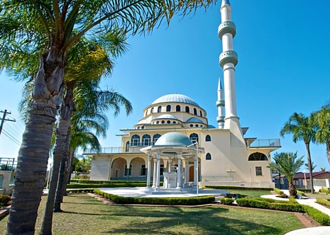 The Auburn Gallipoli Mosque with its cream-coloured dome and minaret surrounded by palm trees and landscaped grounds